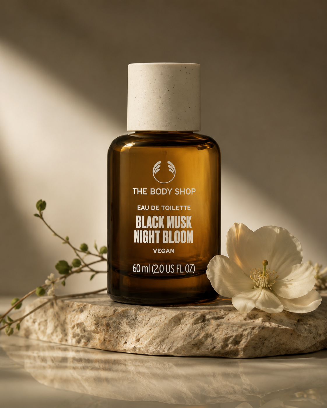 The Body Shop perfume bottle labeled 'Black Musk Night Bloom' on a stone surface with a flower and plant.