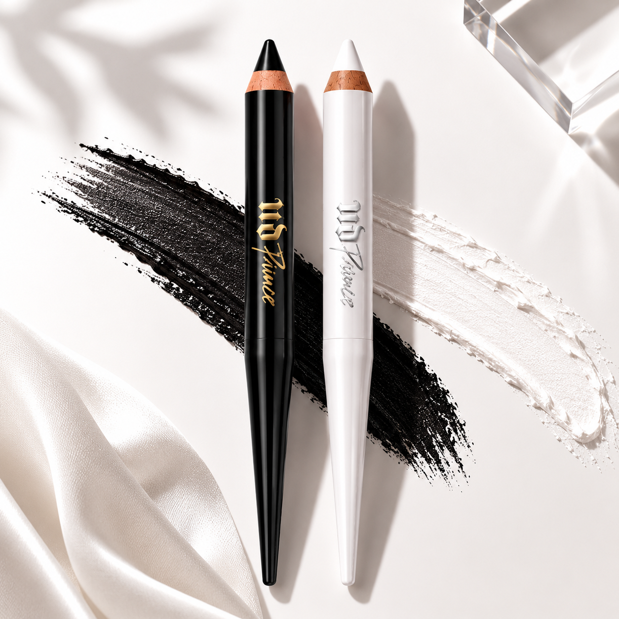 Two makeup pencils, one black and one white, with visible brand name on a white fabric background.